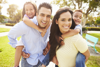 Parents Giving Children Piggyback Ride In Garden. Photo for Seton dentist and SE calgary dentist, Dr Patel to show how vitamin D is good for your teeth and dental care for children.