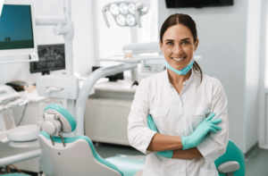 A female dentist standing near a dental chair with her arms crossed