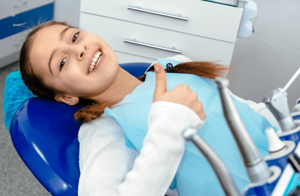 A young girl with her thumbs up after getting her teeth cleaned. She regularly visits her dentist for teeth cleaning and dental check-up