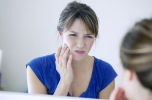 A woman in the mirror touching her jawline due to pain because of her growing wisdom tooth