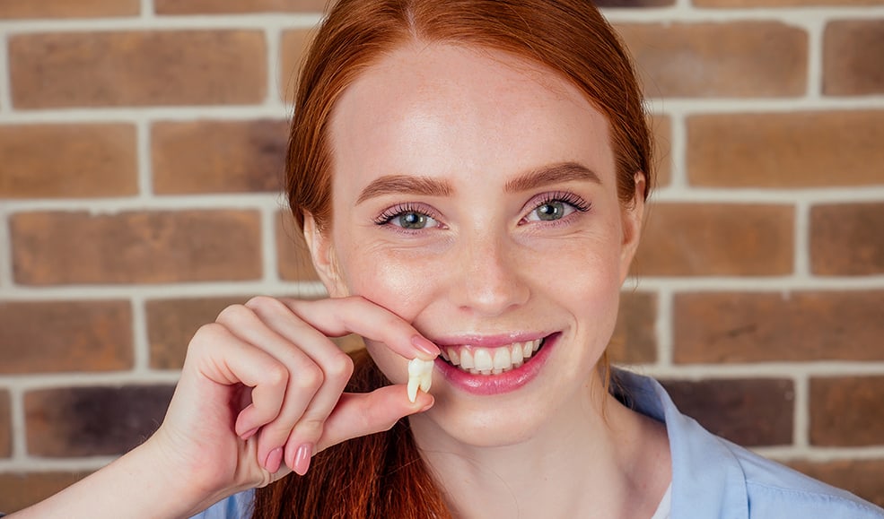 A young woman smiling and holding a plastic model of a tooth next to her mouth