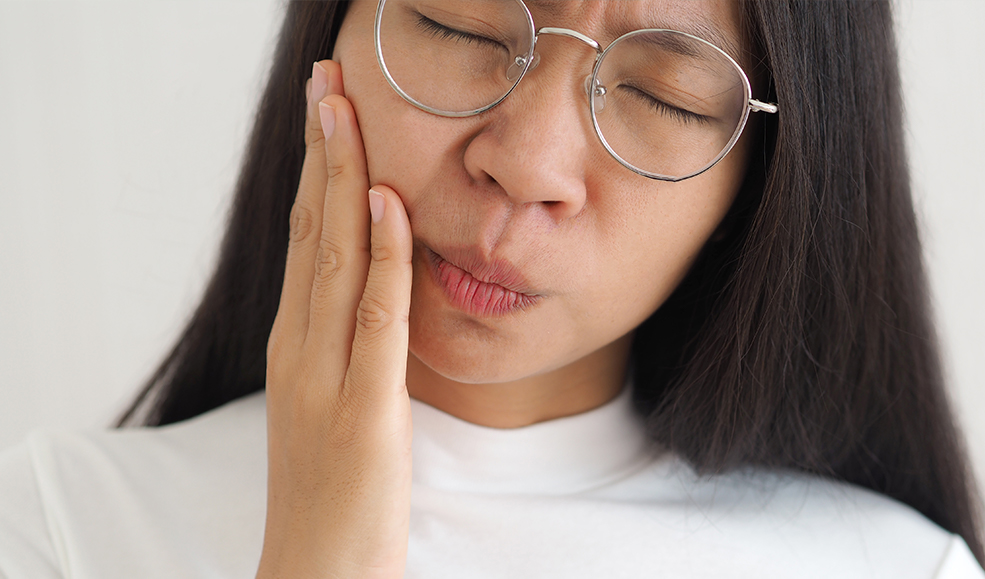 A young woman holds the side of her jaw due to jaw pain from TMJ disorder