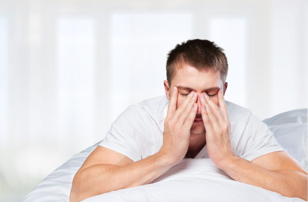 A man lying on his bed with his hands over his face and nose, feeling frustrated due to a sleepless night.