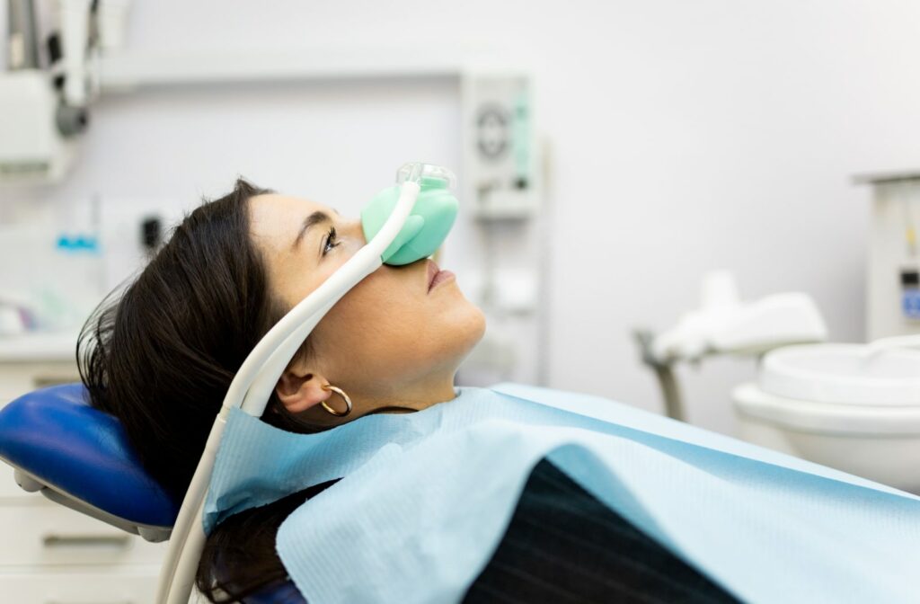 An adult woman sitinng in a dentist's office wearing a nasal mask to inhale nitrous oxide.