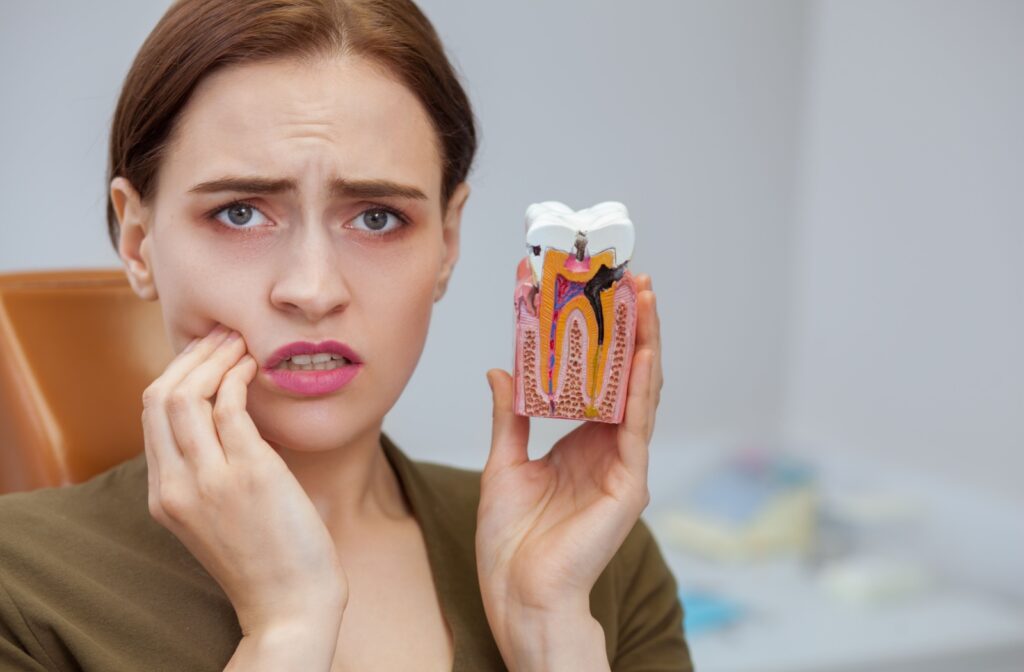 Woman holding her cheek in pain while displaying a model of a tooth with a cavity.