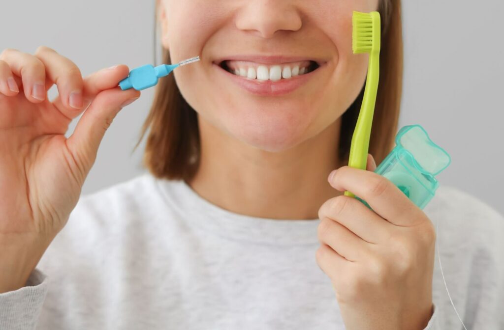 A smiling patient holding their toothbrush, dental floss, and interdental brush.