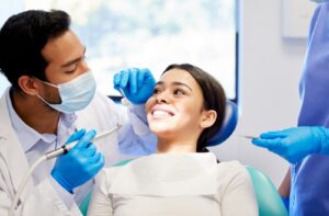 Patient smiles as they sit in their appointment as two dental professionals carry out an exam.